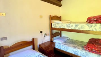 Une chambre avec deux lits superposés, une table de chevet en bois et une prise électrique au mur.