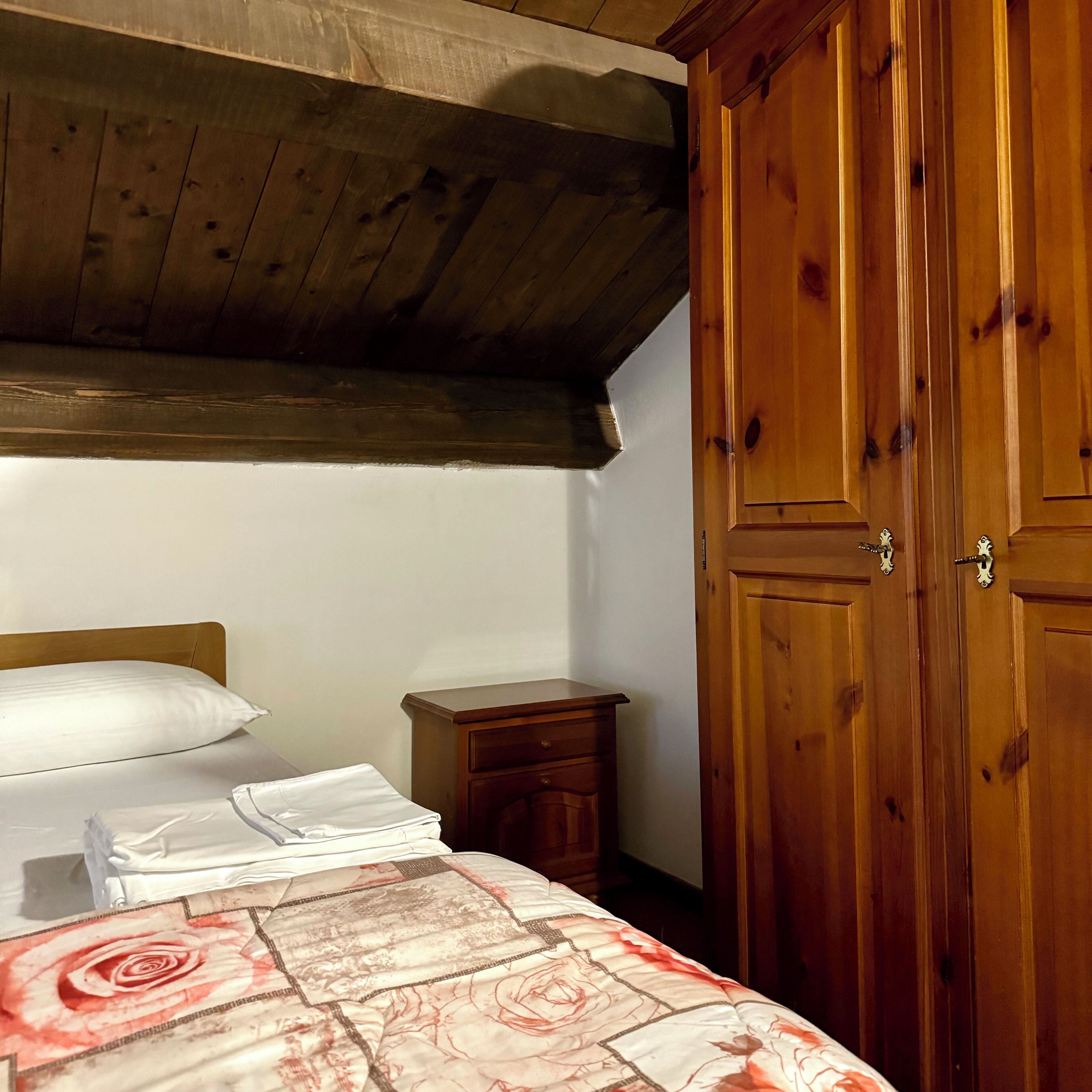 Ein Schlafzimmer mit Holzboden, einem Bett mit floralem Überwurf, einem Nachttisch und einem Holzschrank.