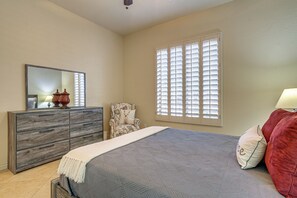 Une chambre à coucher comprenant un lit, une commode, une chaise et une grande fenêtre avec des stores.