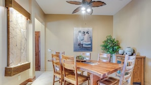 A dining area with a wooden table and chairs, a ceiling fan, a wall-mounted light fixture, and a framed artwork above the table. - Surprise Home w/ Pool & Hot Tub! (Surprise)