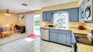 A modern kitchen with blue cabinets, a dishwasher, a microwave, and a stove. There is a dining area with a table and chairs, and a window with curtains. - 7 Mi to Satellite Beach: Melbourne Home w/ Yard (Melbourne)