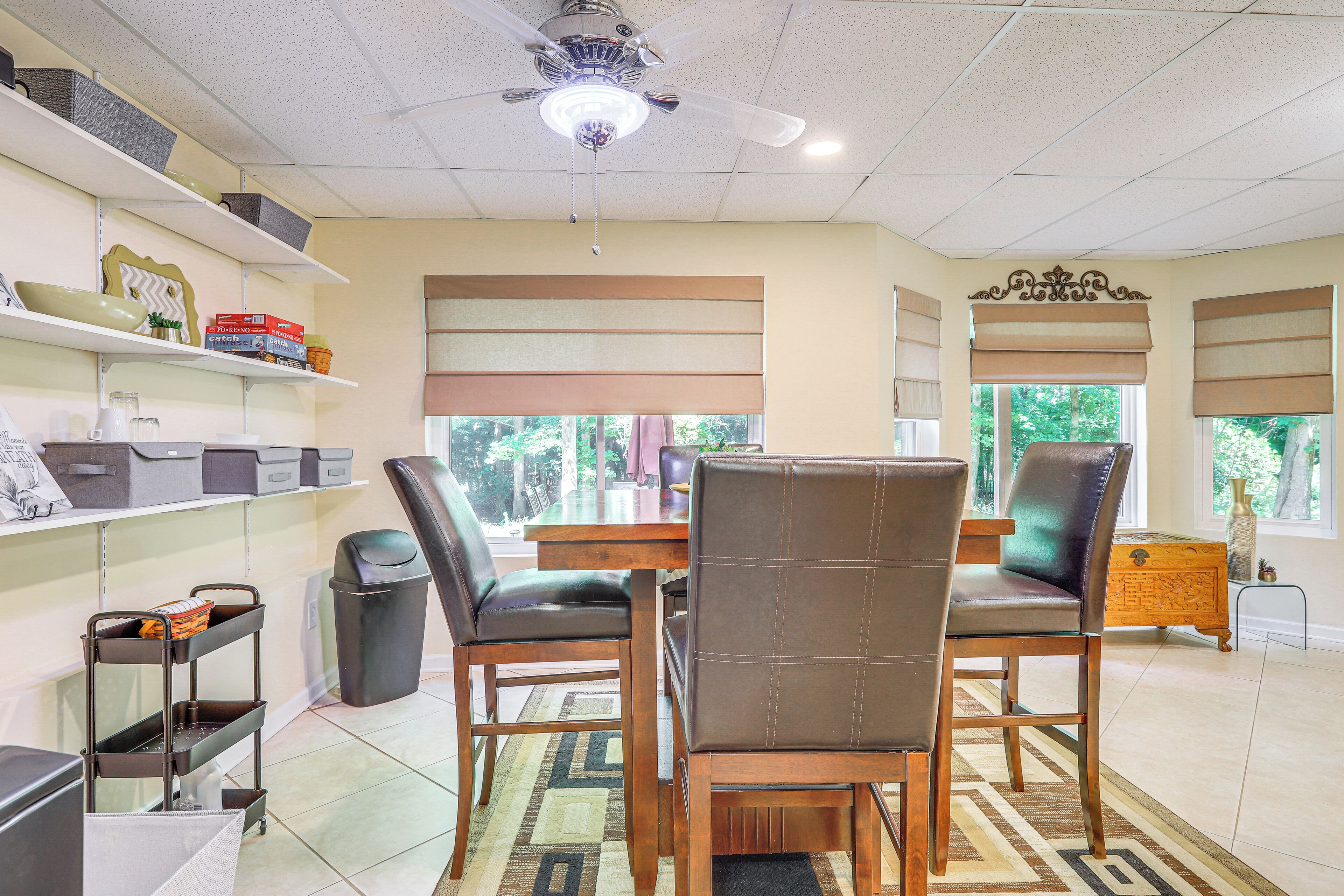 A dining area with a wooden table, two chairs, a ceiling fan, and shelves with storage boxes.