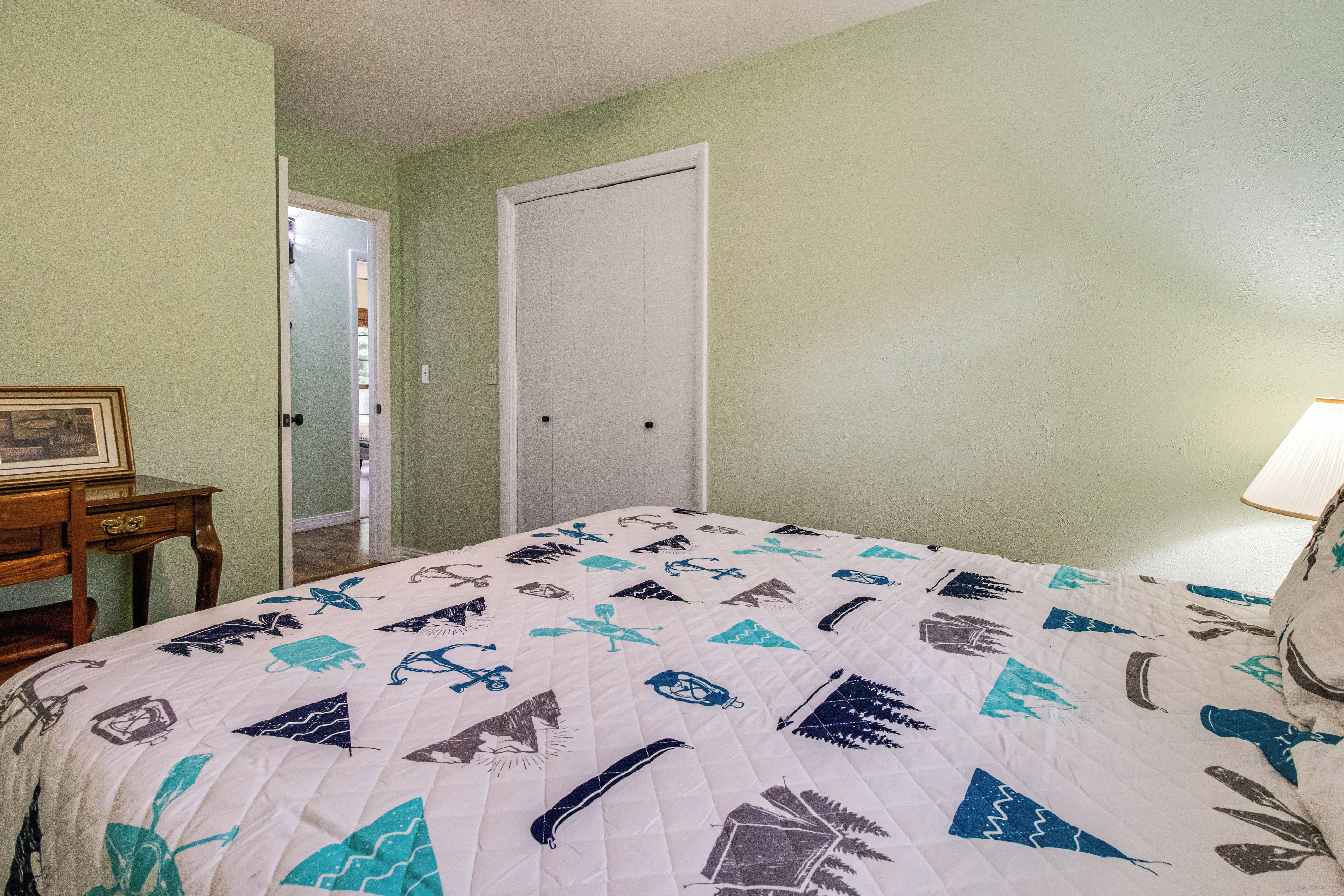 Een slaapkamer met een bed, een nachtkastje, een kaptafel en een deur naar een andere kamer.