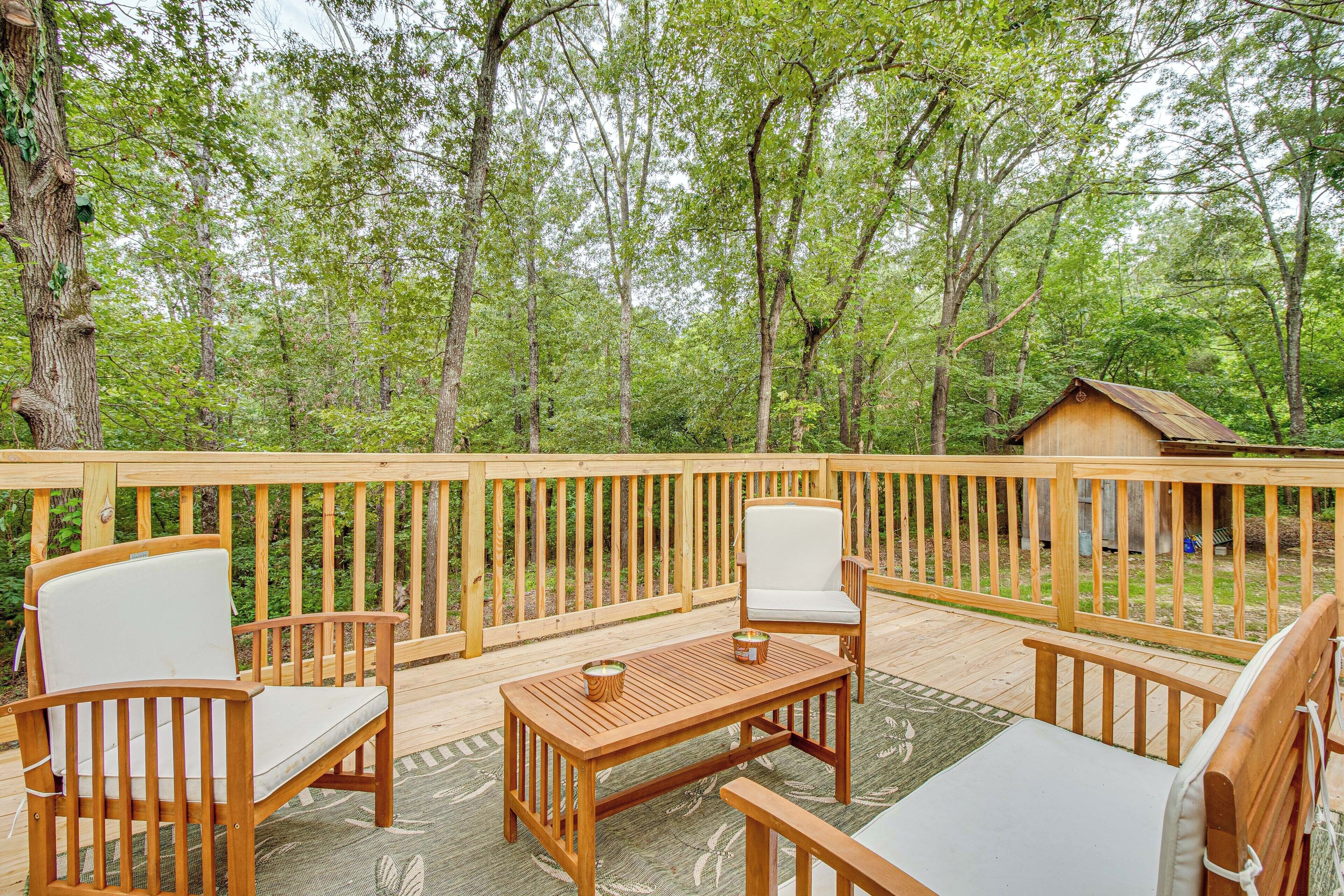 Eine Holzterrasse mit Gartenmöbeln, darunter Stühle und ein Tisch, umgeben von Bäumen.