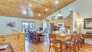 A spacious kitchen with wooden cabinets, a central island, and a dining area with chairs. - Lead Home in the Mountains w/ Hot Tub + Views! (Lead)