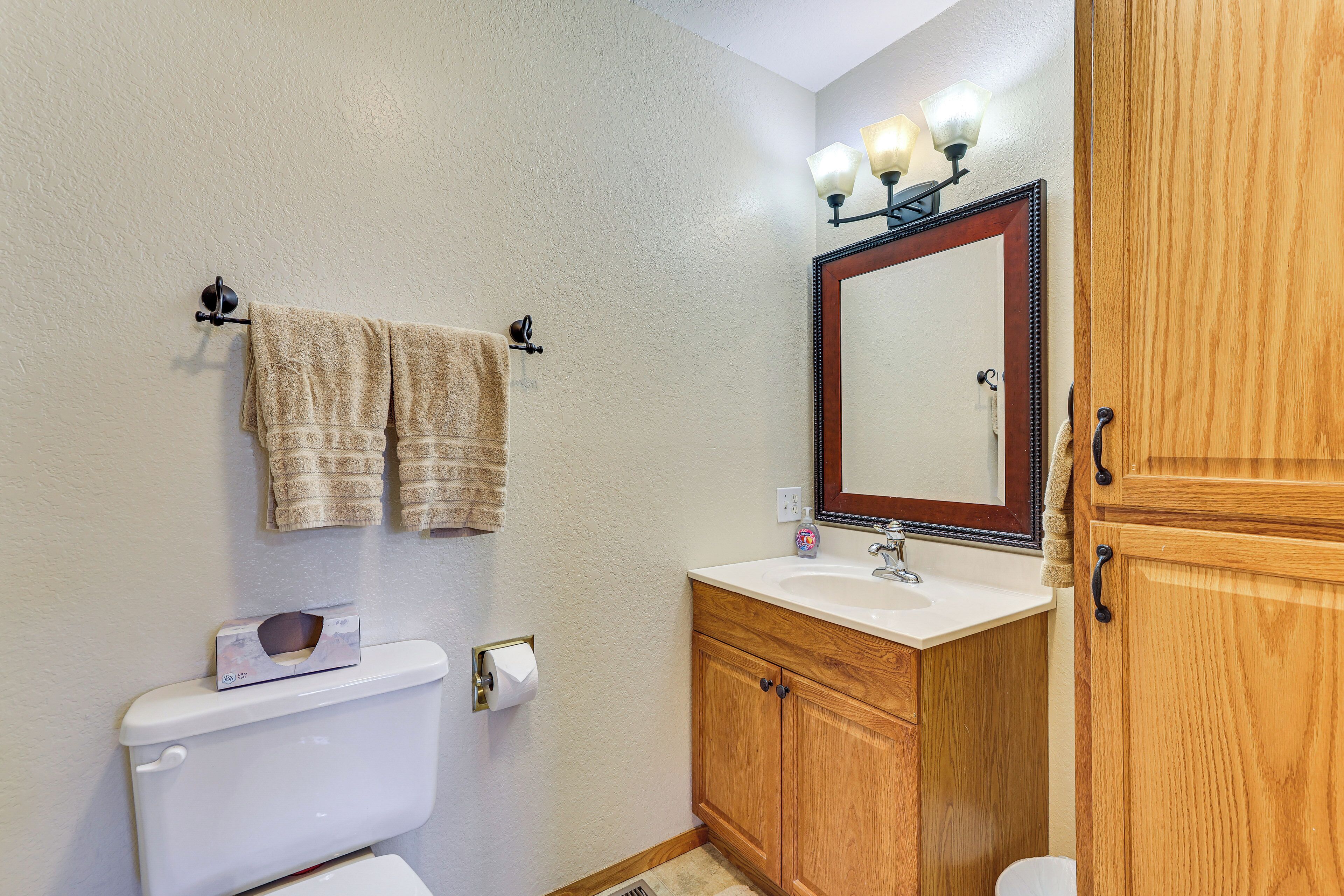 A bathroom with a toilet, sink, wooden cabinets, a mirror with lights, and a towel rack.
