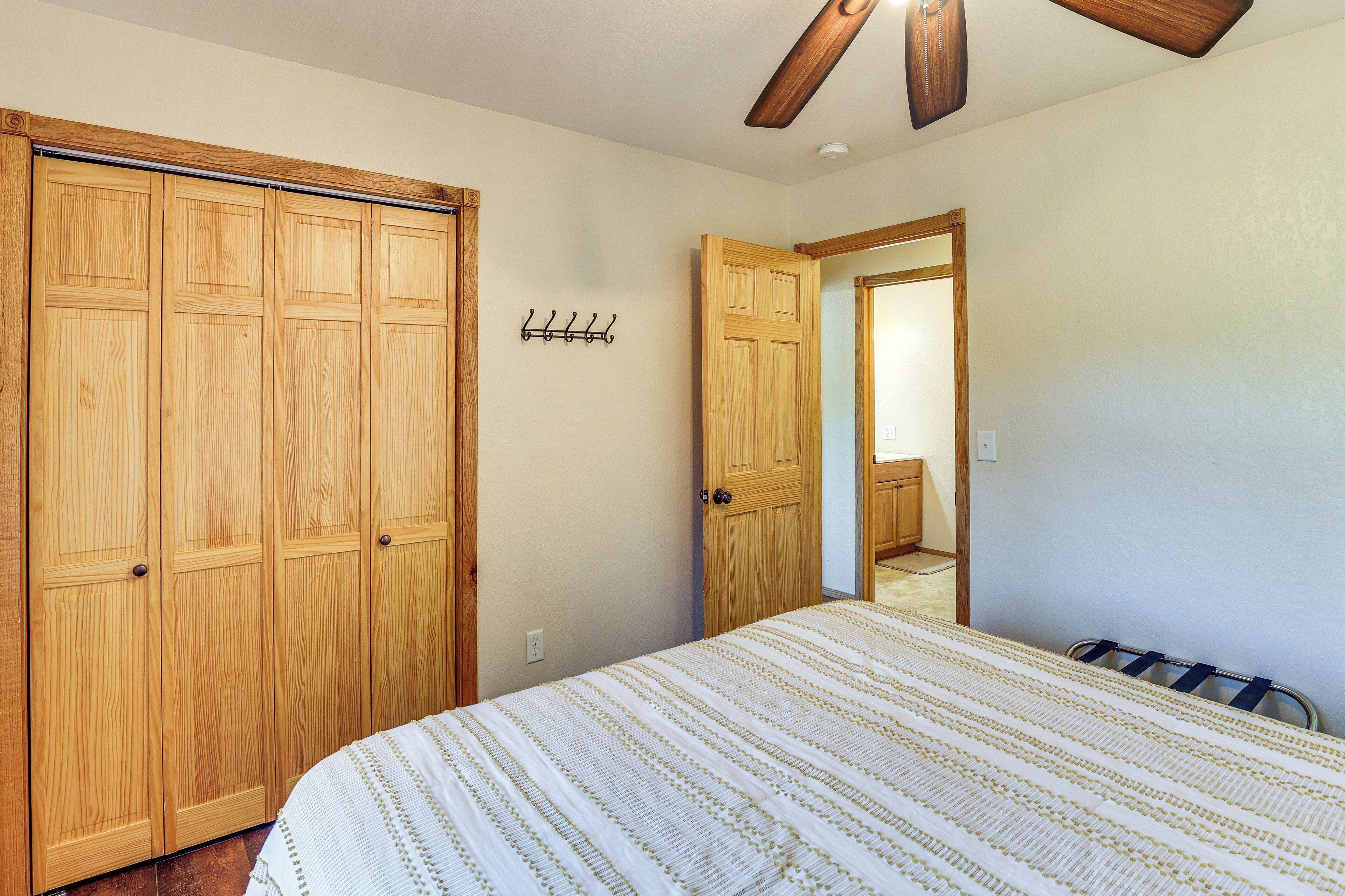 Un dormitorio con un armario de madera, una cama con colcha a rayas y un ventilador de techo.