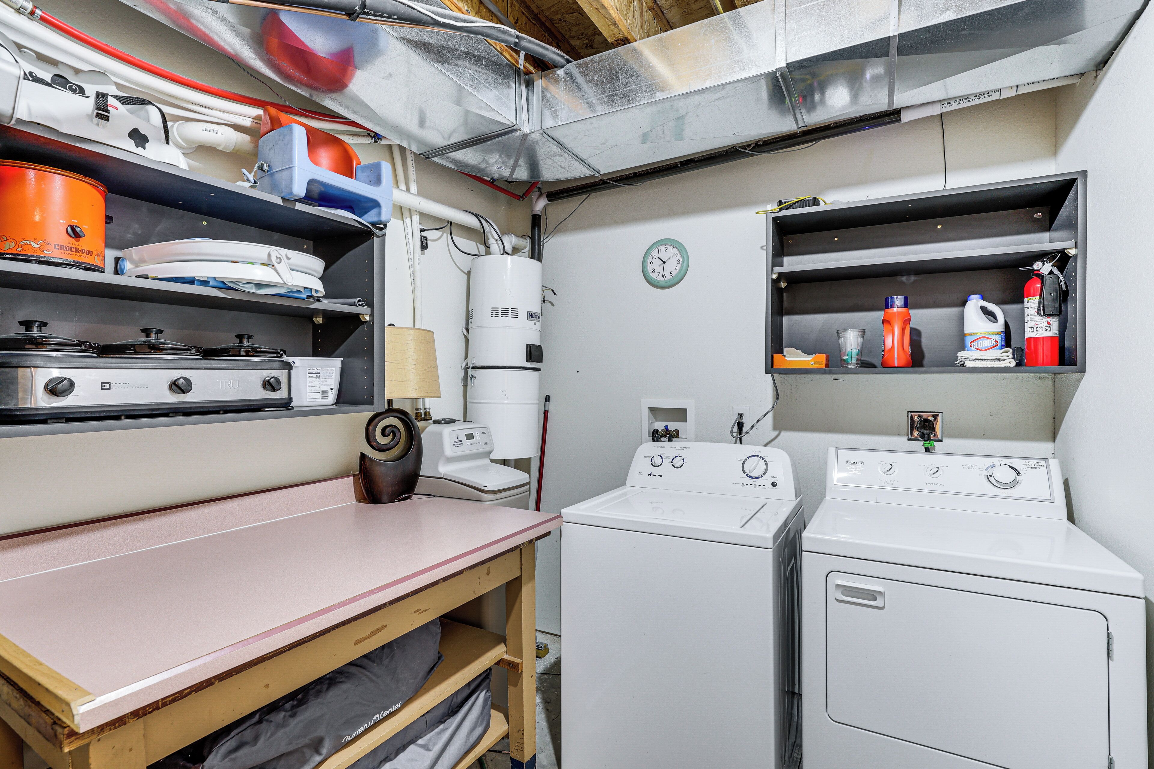 A compact laundry room with a washing machine, dryer, and shelves with various items.