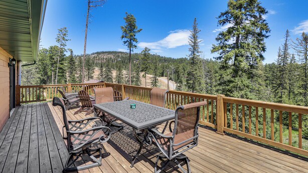 A wooden deck with a table and chairs, overlooking a forested area. - Lead Home in the Mountains w/ Hot Tub + Views! (Lead)