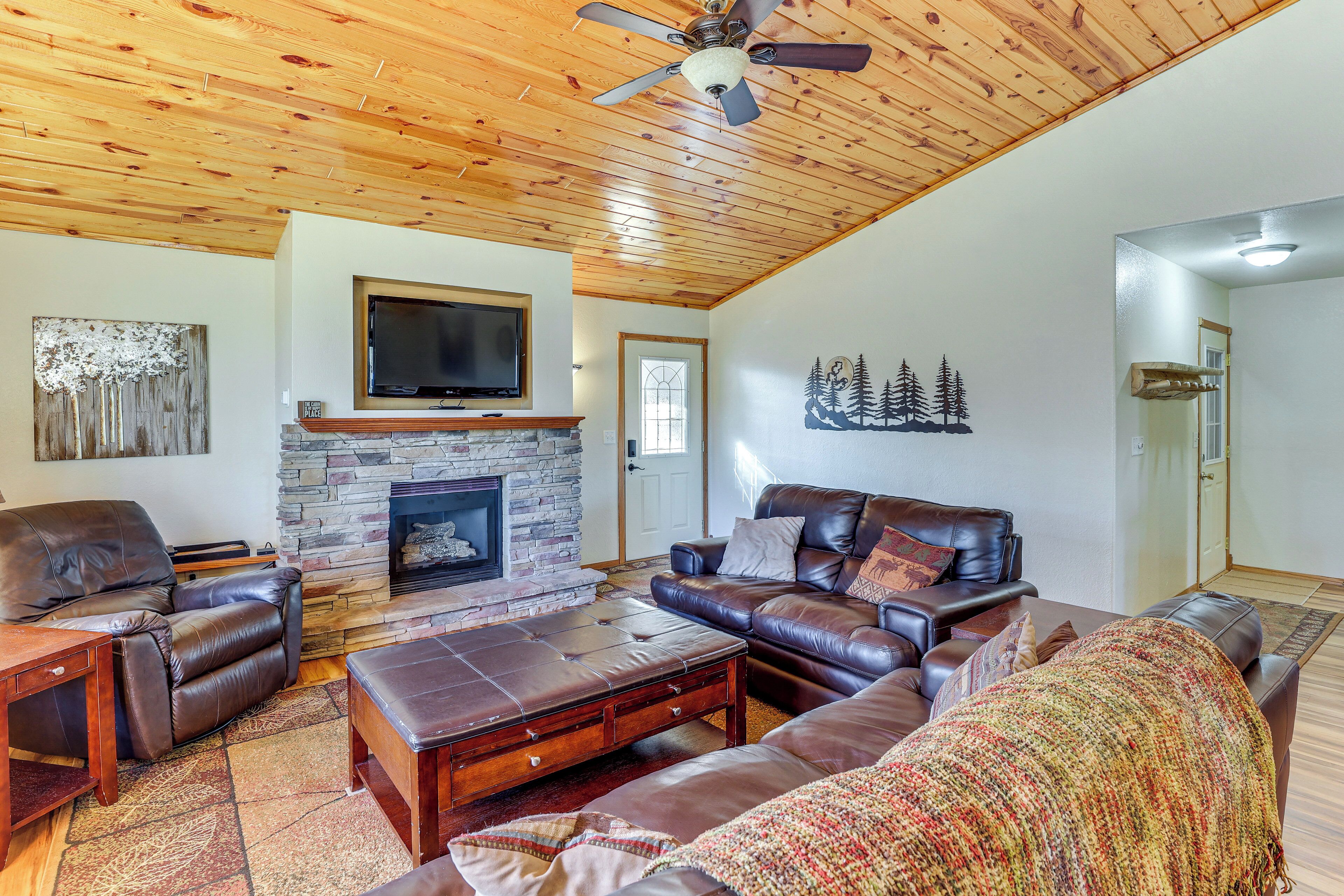 A living room with leather sofas, a stone fireplace, a flat-screen TV, and a ceiling fan.