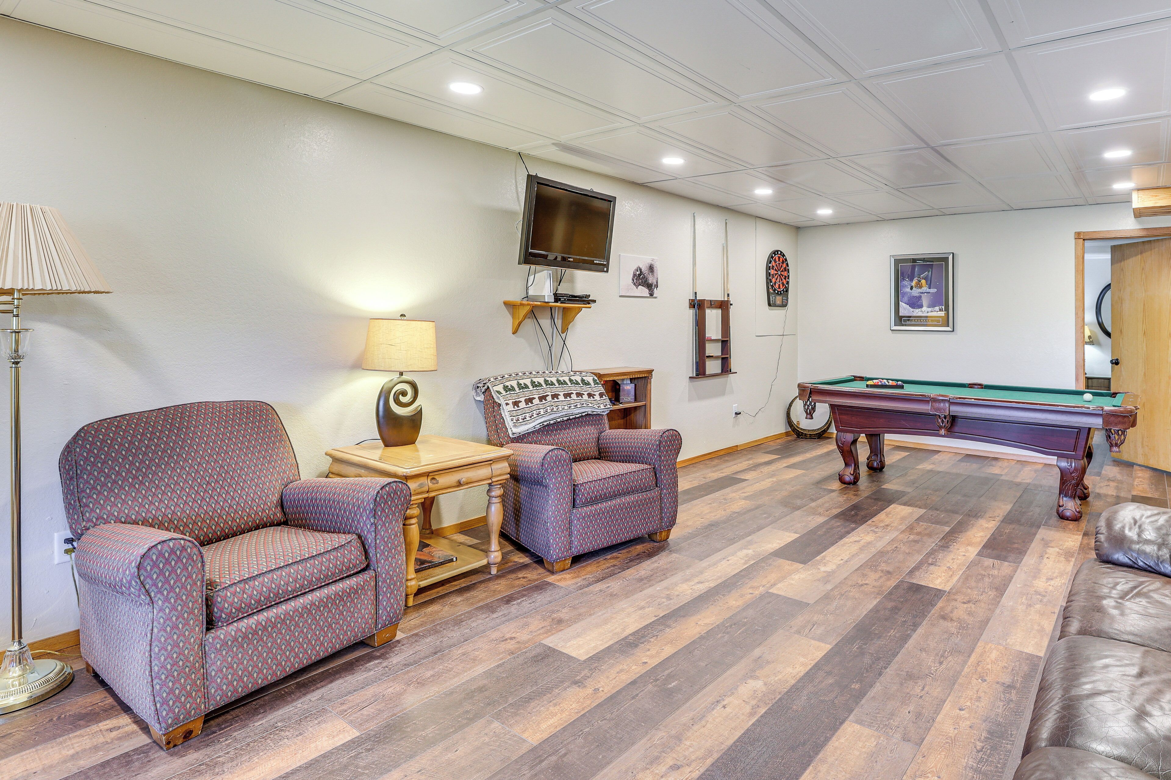 Une pièce avec une table de billard, deux fauteuils à motifs, une lampe et un téléviseur fixé au mur.