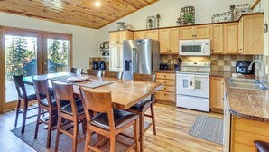 A spacious kitchen with wooden cabinets, a stainless steel refrigerator, a microwave, and a stove. There is a dining area with a wooden table and chairs. - Lead Home in the Mountains w/ Hot Tub + Views! (Lead)