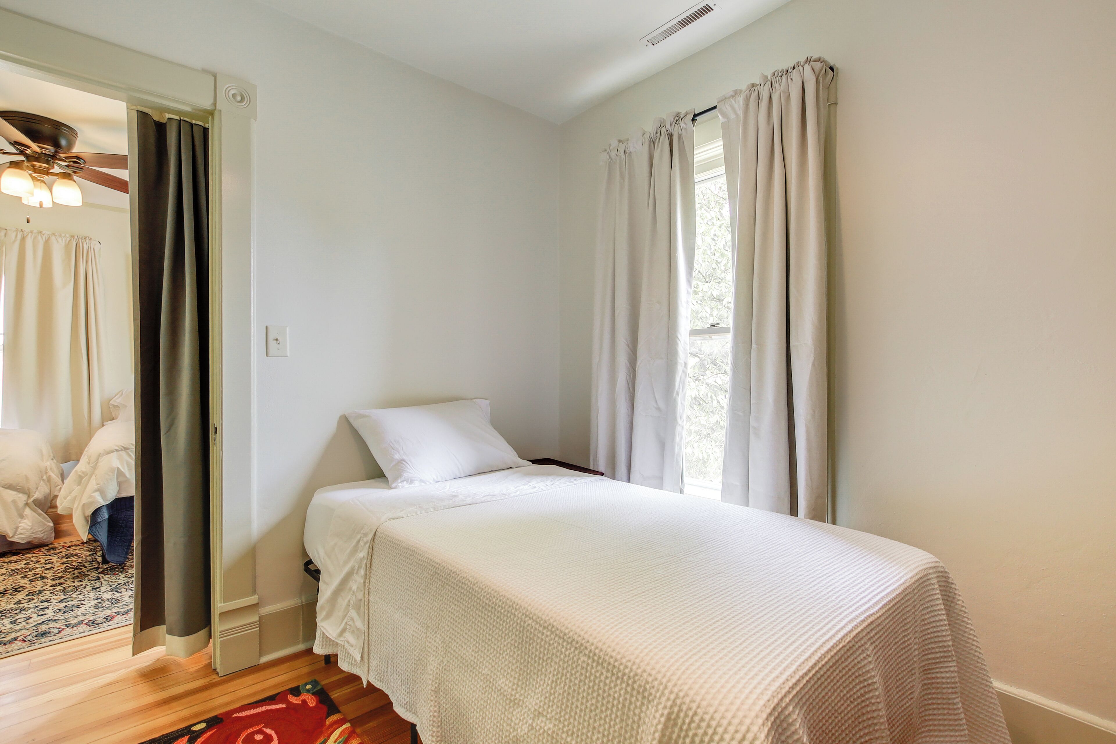 A bedroom with a single bed, a ceiling fan, and a window with curtains.