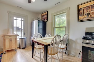 A kitchen with a dining table, chairs, a refrigerator, a trash can, and a stove.