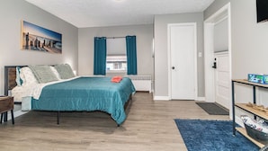 A bedroom with a bed, a nightstand, a blue rug, a door, and a window with curtains.
