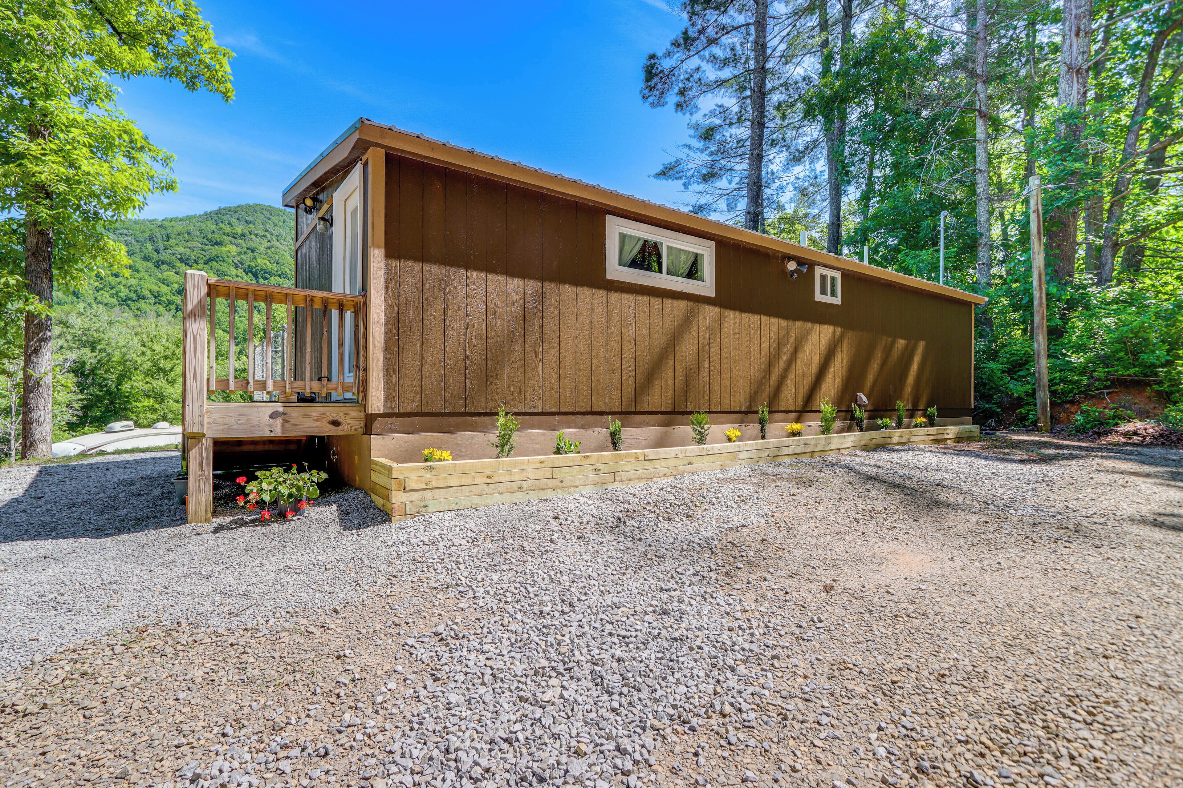 A wooden cabin with a deck, surrounded by gravel and greenery.