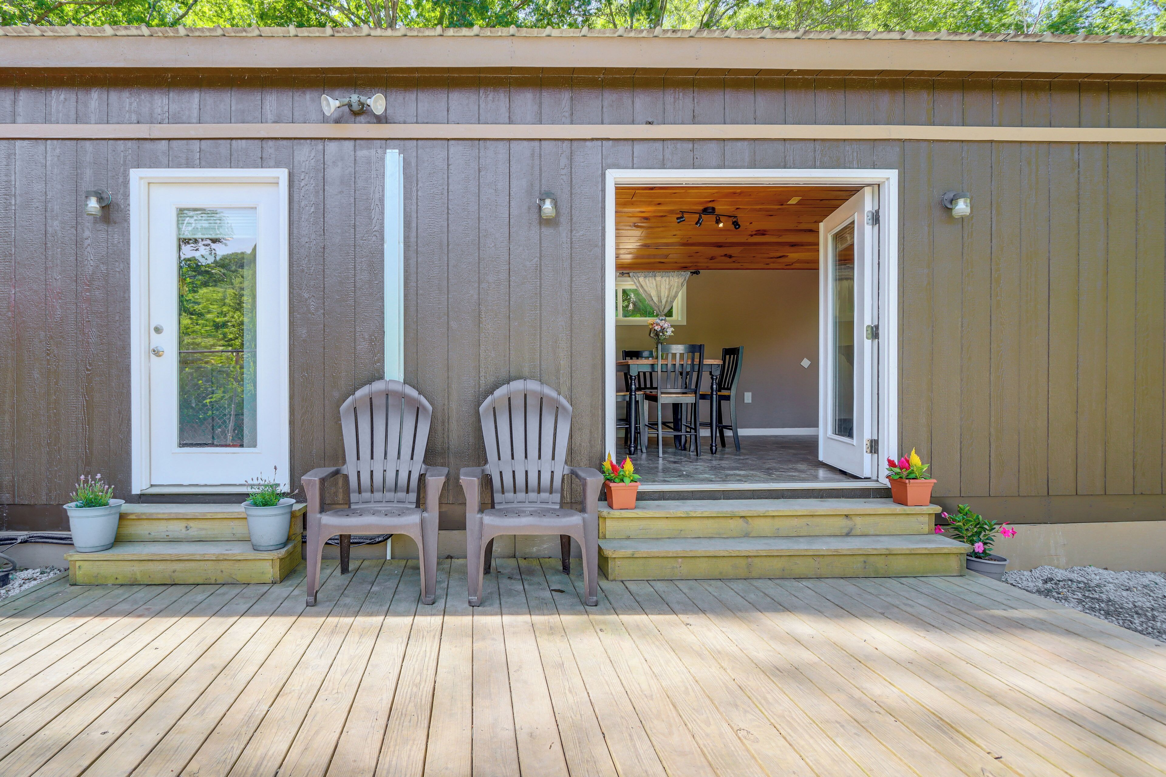 A wooden deck with two chairs and potted plants, leading to a covered patio area with a table and chairs.