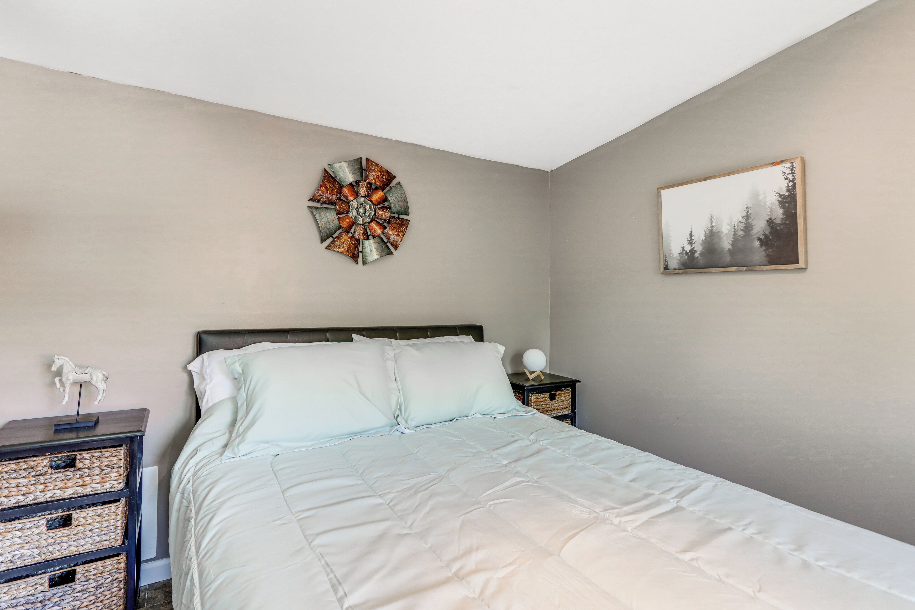 A bedroom with a bed, a wall clock, a framed picture, and a nightstand with baskets.