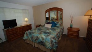 Une chambre à coucher comprenant un lit, une télévision, une commode, une table de chevet, une lampe et un miroir.