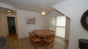 Une salle à manger avec une table et des chaises en bois, un ventilateur de plafond et un tableau au mur.