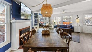 Een ruime eethoek met een houten tafel en stoelen, een hangende geweven lamp en een uitzicht op het omliggende landschap door grote ramen.