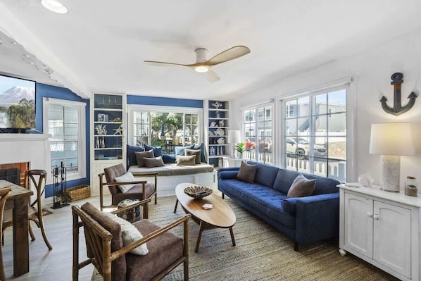 A spacious living room with a blue sofa, wooden chairs, a coffee table, and a ceiling fan.