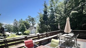 An outdoor deck with a table and chairs, surrounded by a wooden deck and a patterned rug. - Daybreak Limit 8 3 Bedroom Villa by RedAwning (Sebago)
