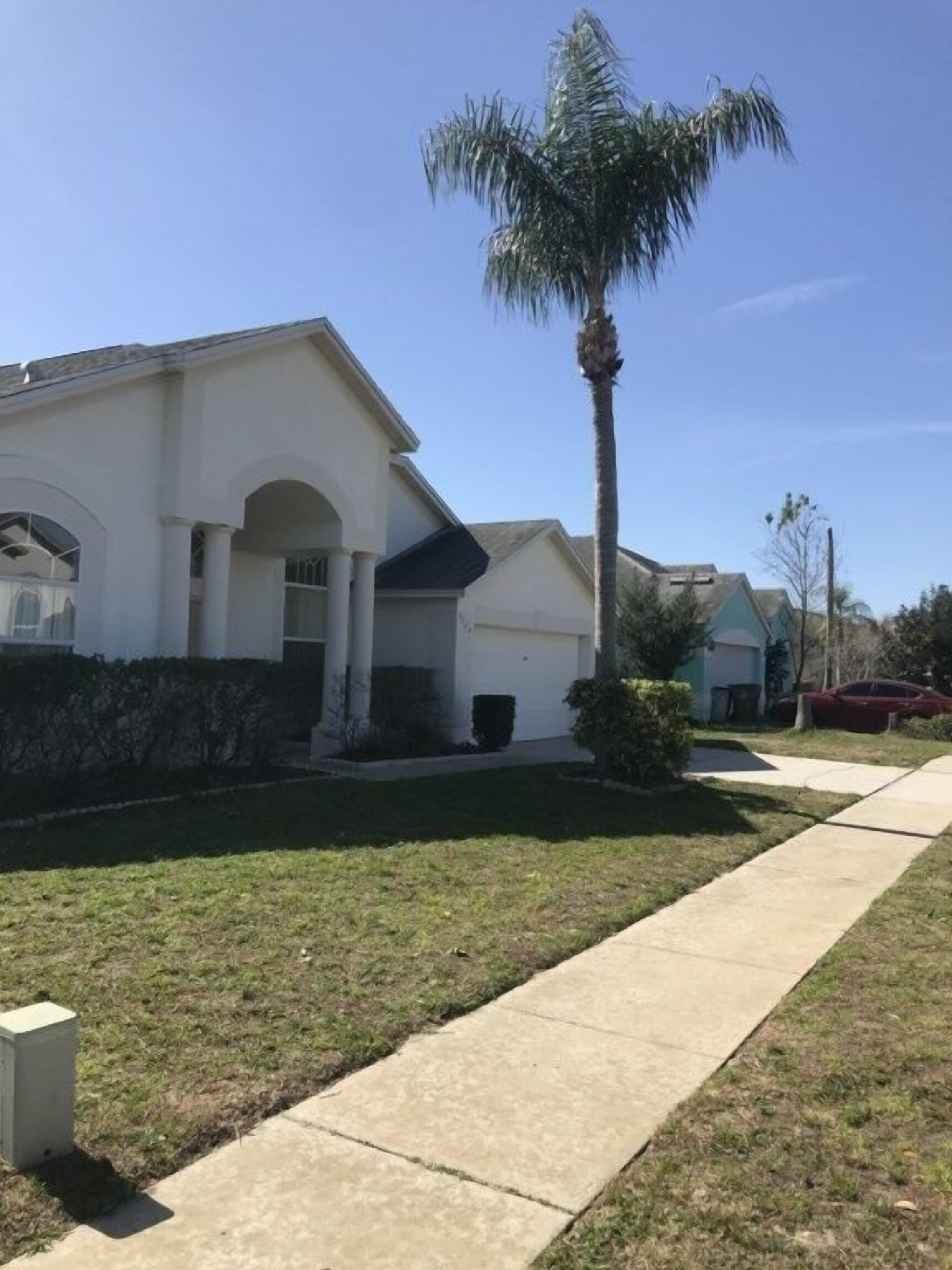 A residential house with a well-maintained lawn, a sidewalk, and a palm tree.