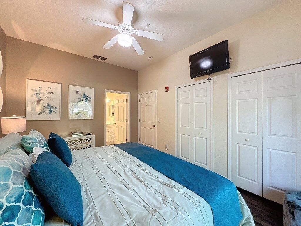 Ein Schlafzimmer mit einem Bett, Deckenventilator, Fernseher und weißen Türen.