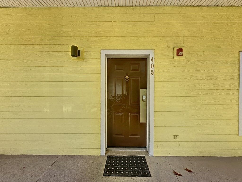 A yellow building with a brown door, number 405, and a small red sign above it.