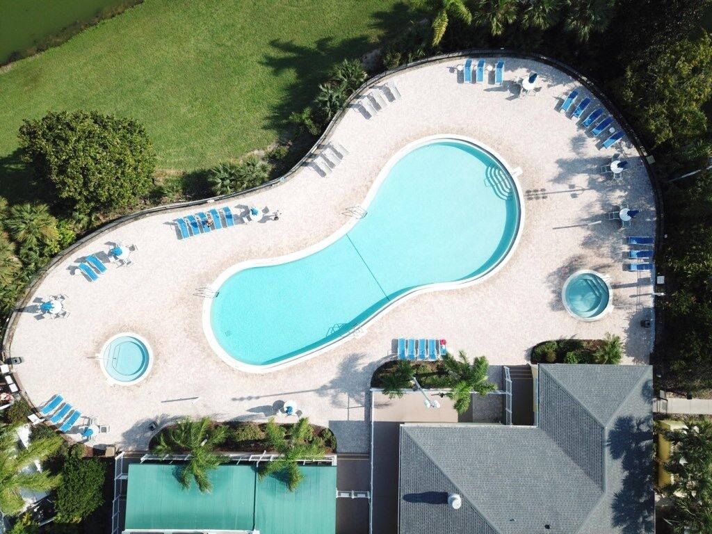 An aerial view of a resort with a large swimming pool, multiple lounge areas, and a separate pool for children.