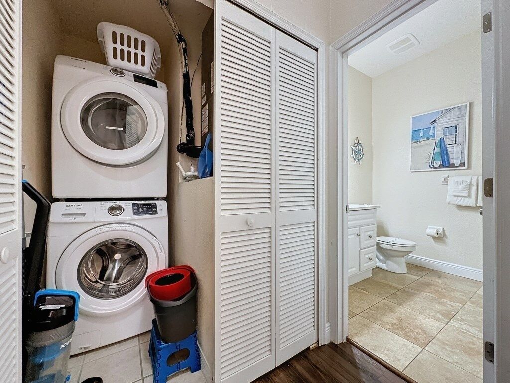 A laundry area with two washing machines, a drying rack, and a trash bin.