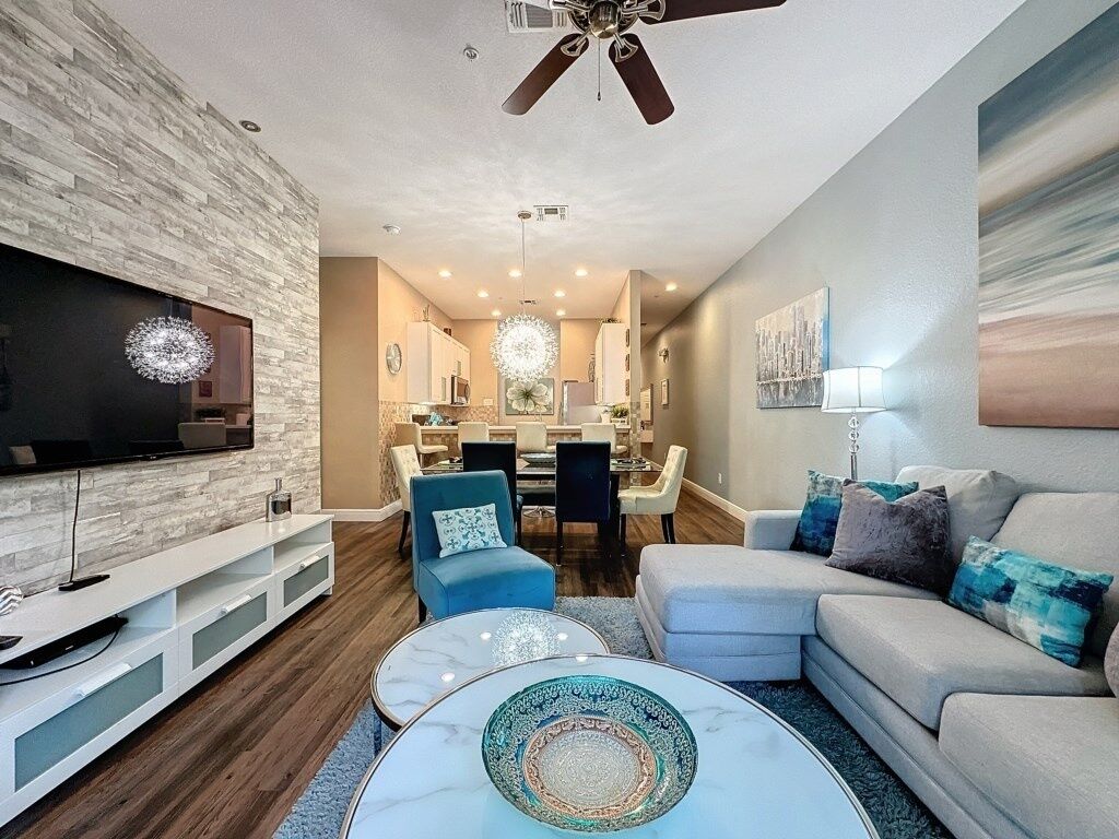 A modern living room with a flat-screen TV, a ceiling fan, and a dining area with a chandelier.