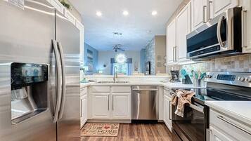 A modern kitchen with stainless steel appliances, white cabinetry, and a wooden floor.