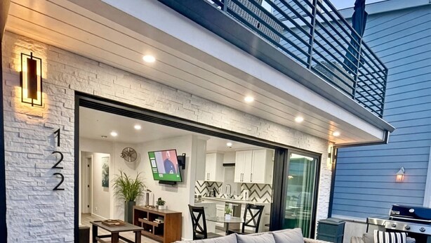 A modern outdoor living area with wicker furniture, a glass door leading to a kitchen, and a balcony with a railing.
