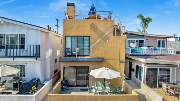 Un edificio de dos plantas con balcón, mobiliario exterior y una escalera.