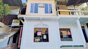 Un edificio de dos pisos con un letrero que indica que es un hotel. Se ve una escalera que conduce a la entrada, y un letrero de Mushola.