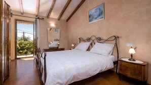 A bedroom with a wooden bed, bedside lamps, a mirror, and a view of a garden through an open door. - Typical Istrian stone house,6 persons,beautiful panoramic view of the sea,garden (Kastelir)