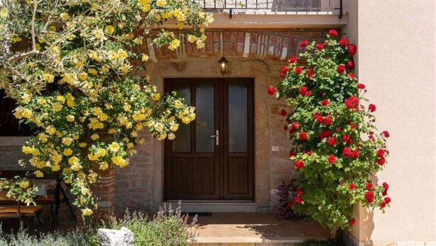 A building with a wooden door, a balcony, and a garden with yellow and red flowers. - Typical Istrian stone house,6 persons,beautiful panoramic view of the sea,garden (Kastelir)