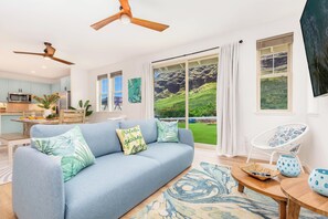 A modern living room with a blue sofa, a dining area with a wooden table, and a kitchen with a microwave. - Ocean Views Serene Vacation Escape Home Near Beach w/Beach Equipment & Games (Waianae)