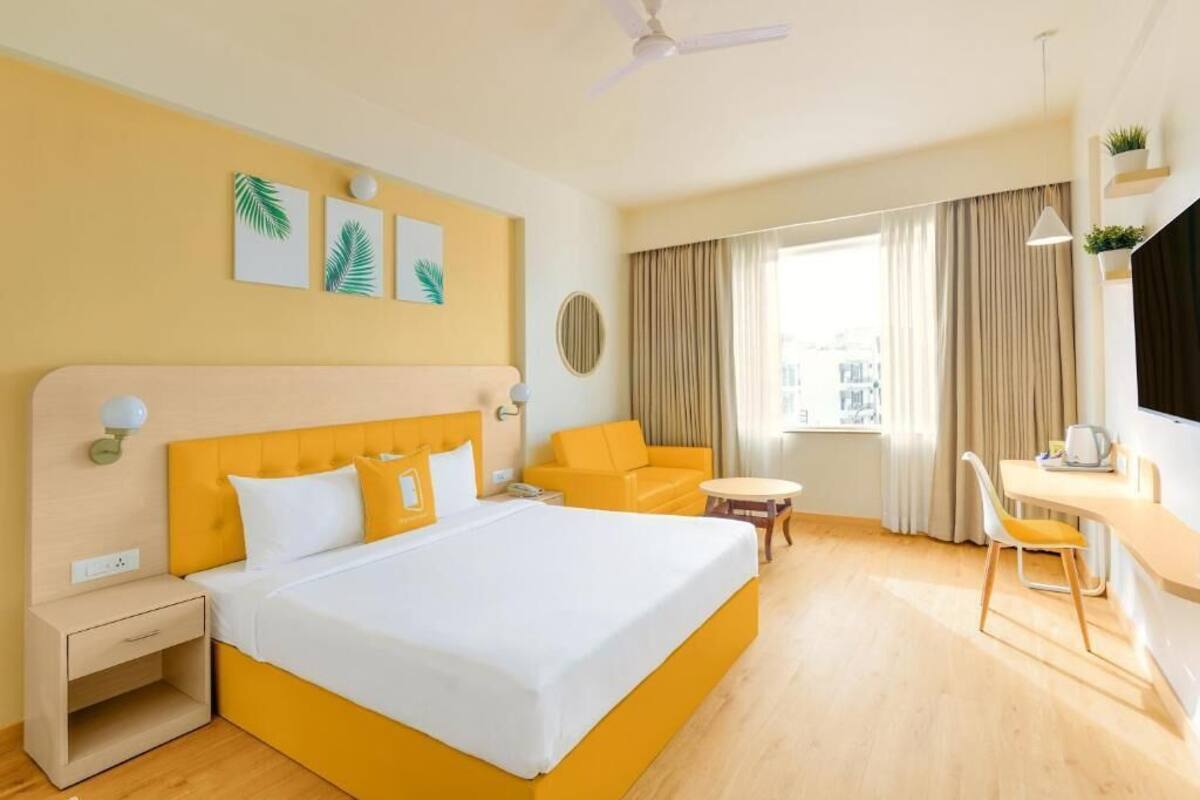 A hotel room with a bed, a desk, a chair, a small table, a sofa, and a window with curtains.