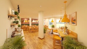 Un comedor amplio con suelo de madera, varias mesas y sillas, y lámparas colgantes amarillas.
