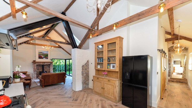 A spacious kitchen with a herringbone floor pattern, wooden cabinets, a black refrigerator, and a stone fireplace.