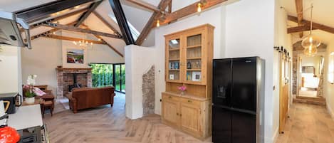 Une cuisine spacieuse avec un parquet à motifs en chevrons, des meubles en bois, un réfrigérateur noir et une cheminée en pierre.