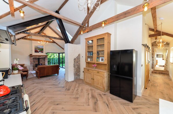 A spacious kitchen with a herringbone floor pattern, wooden cabinets, a black refrigerator, and a stone fireplace.