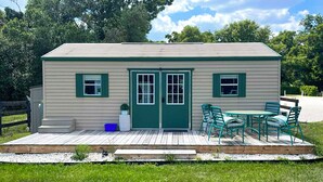 Una piccola casa con una porta verde, due finestre e un patio con sedie.