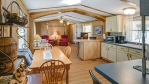 A cozy kitchen with wooden cabinets, a dining area with a table and chairs, and a small island with a microwave. - Blackwell Home w/ Enclosed Porch: Steps to Water! (Blackwell)