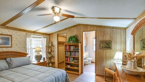 A bedroom with a bed, a wooden headboard, a ceiling fan, a bookshelf, a desk, and a mirror. - Blackwell Home w/ Enclosed Porch: Steps to Water! (Blackwell)