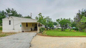 A single-story building with a porch, a gravel driveway, and a grassy yard with trees. - Blackwell Home w/ Enclosed Porch: Steps to Water! (Blackwell)