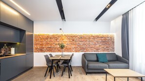 Una cocina moderna con armarios oscuros, una zona de comedor con mesa y sillas de madera, un sofá gris y una pared de ladrillo.